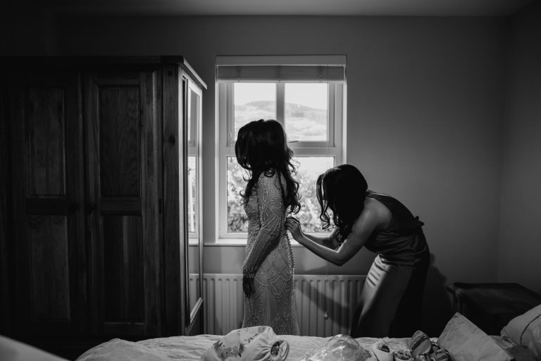 bride getting dressed with bridesmaid help in black and white