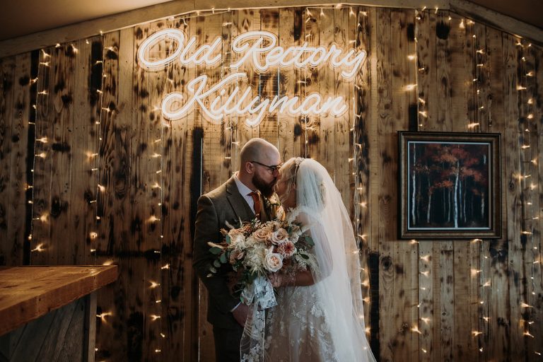 bride and groom kissing under the Old Rectory Killyman sign with fairy lights.