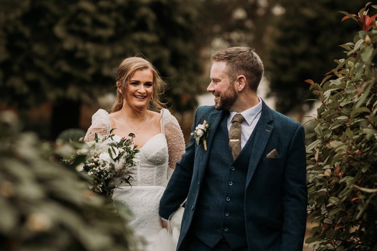bride and groom walking through foliage looking at each other