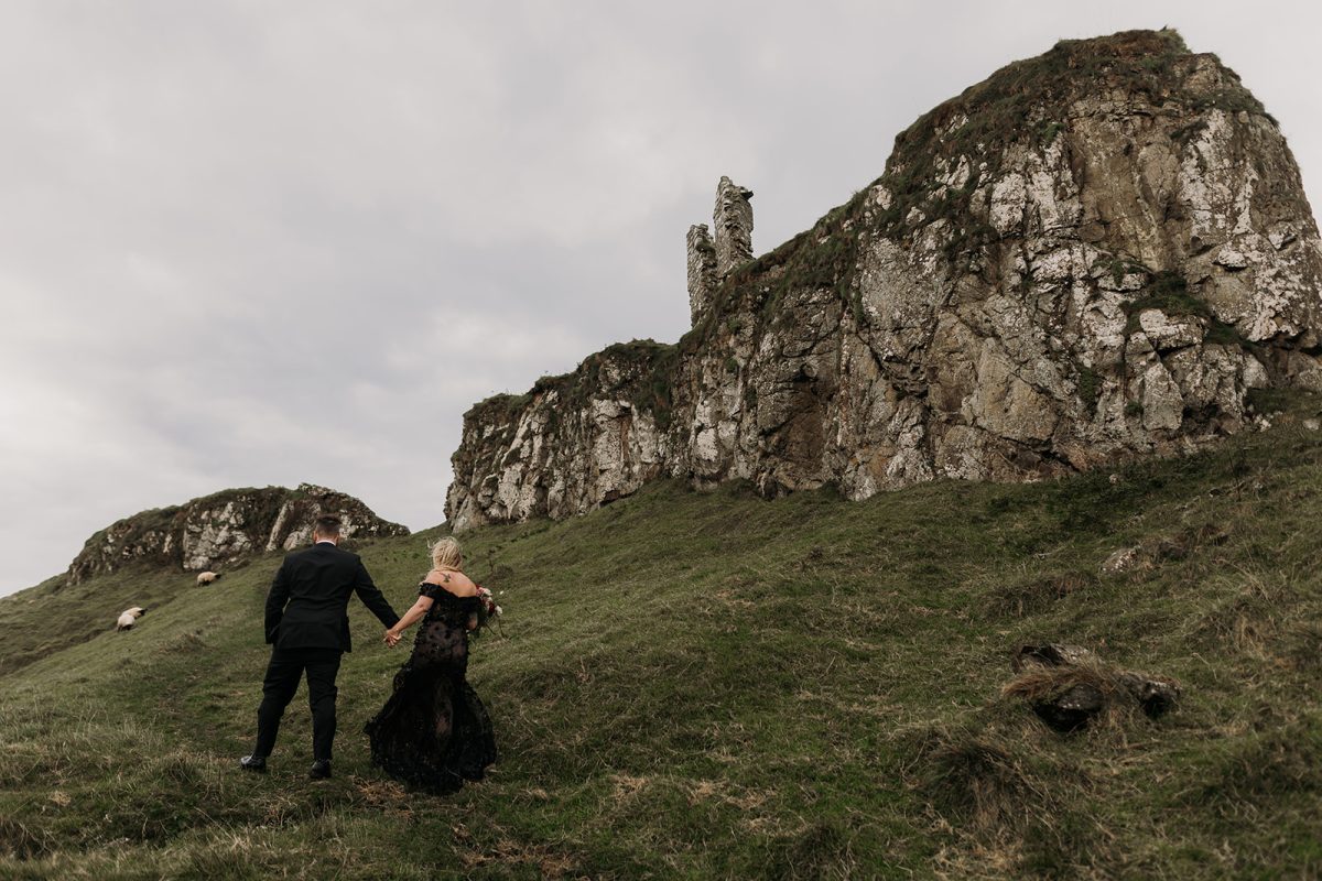 couple walking up green grass field on cliff with sheep