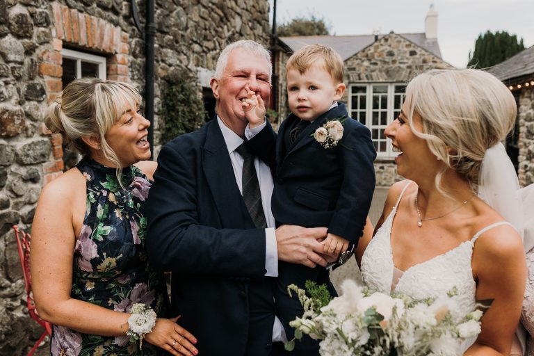 bride with family. the brides young nephew sticks his fingers in his grandads nose. everyone is laughing