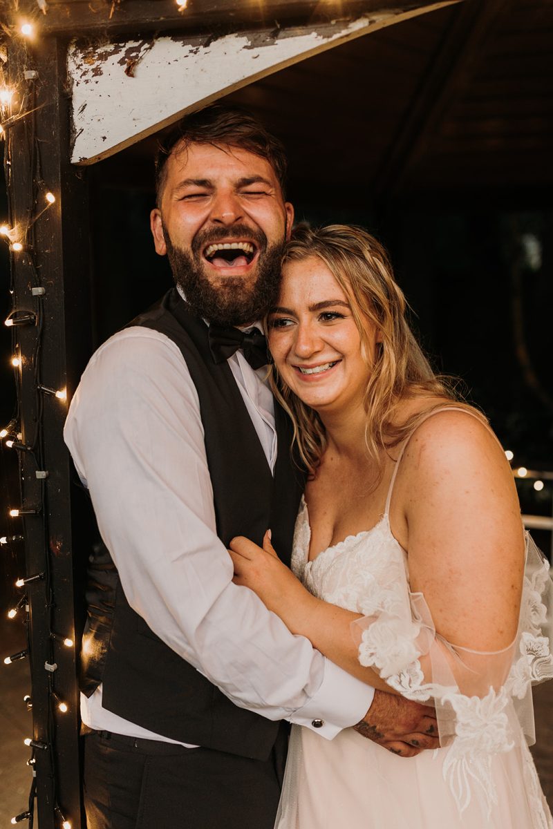bride and groom cuddling and groom has his head lifted back laughing