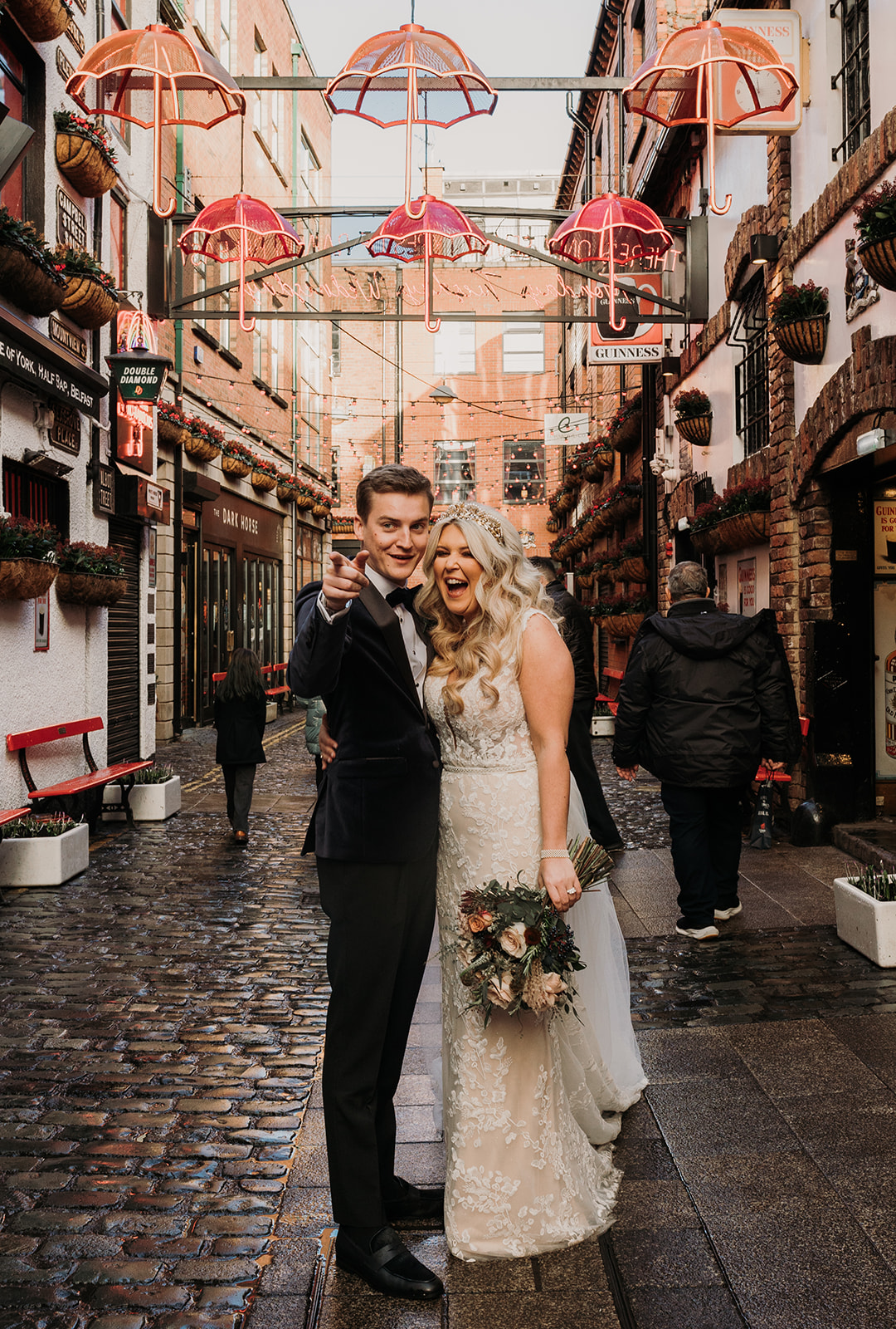 bride and groom at the umbrella display at teh Duke of York pub in Belfast. Groom is pointing and bride is laughing