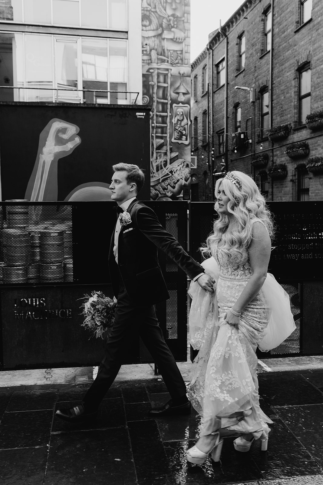 stylish bride and groom walking in Belfast streets. Groom holding flowers.