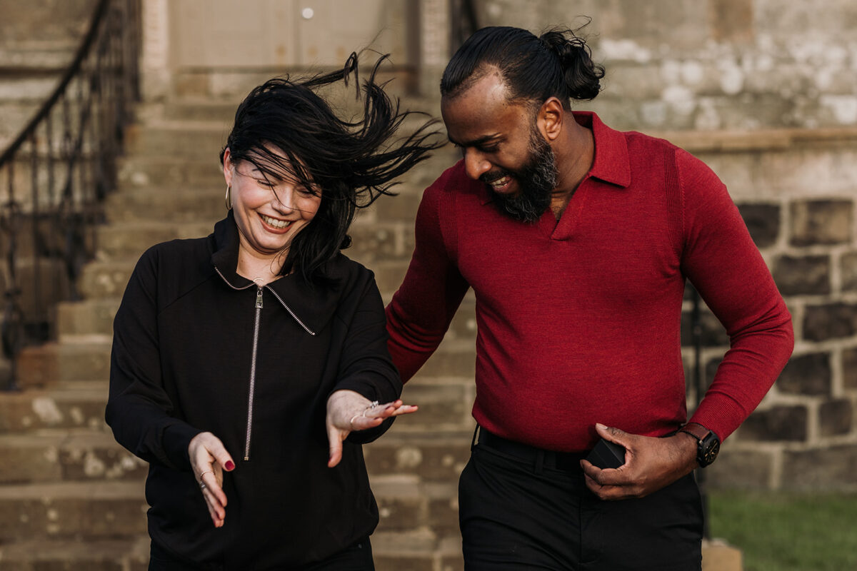 couple at Mussenden temple just got engaged. The couple are looking at her new engagement ring on her hand as the wind blows her hair.