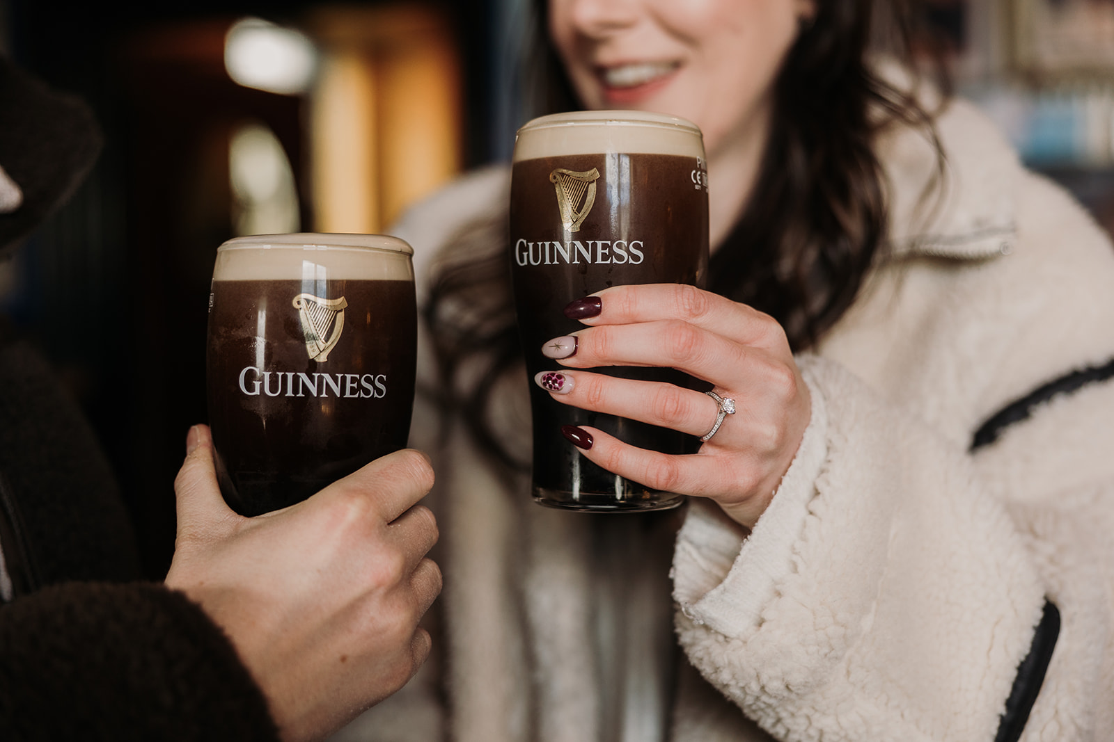 close up photo showing couple with pints of Guinness in their hands showing off her engagement ring.