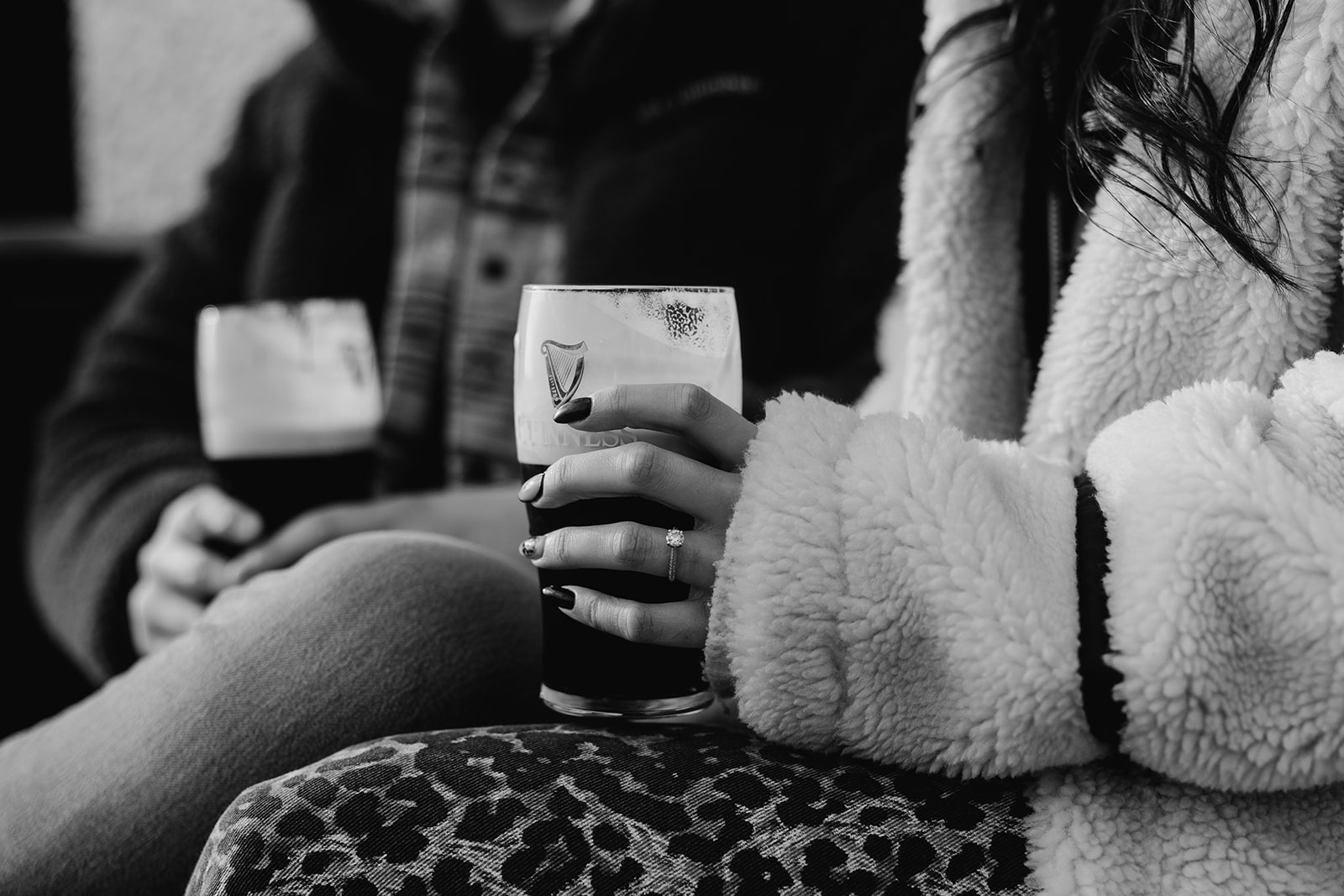 close up showing hands of couple with engagement ring while holding pints of Guinness.