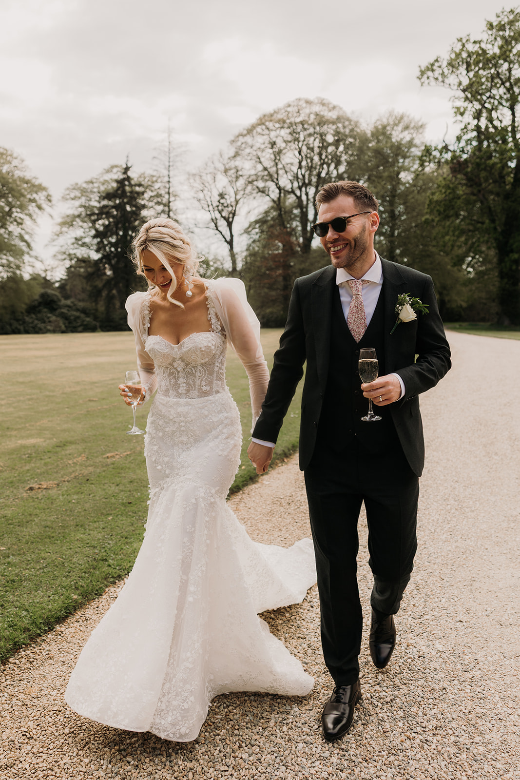 married bride and groom waking with drinks hand in hand