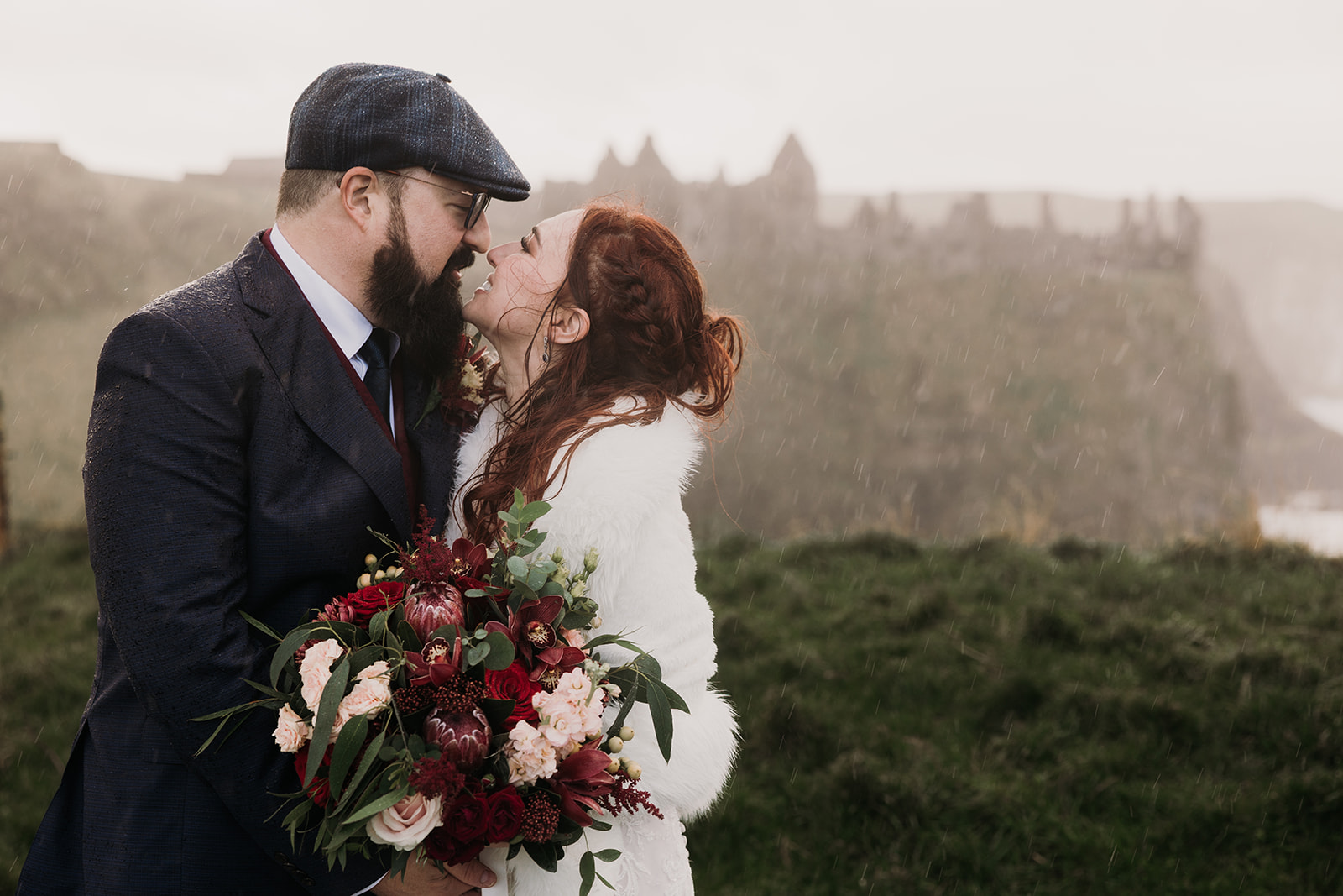 bride and groom eloped. Dunluce castle in back ground. it is raiig hevay, couple are totally soaked with wet hair while kissing.